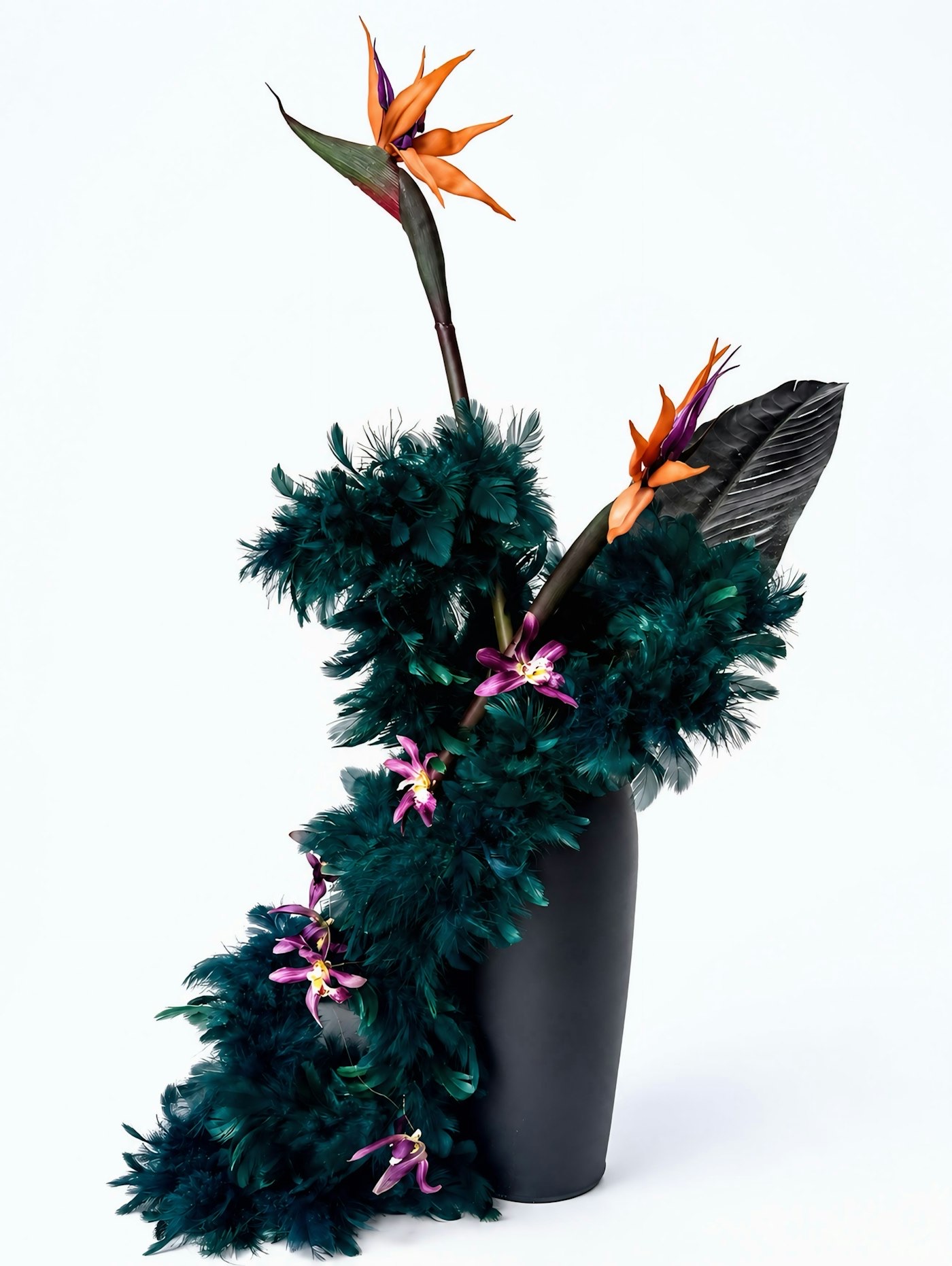 Sculptural arrangement of bird of paradise and dark feathered foliage in a black vase